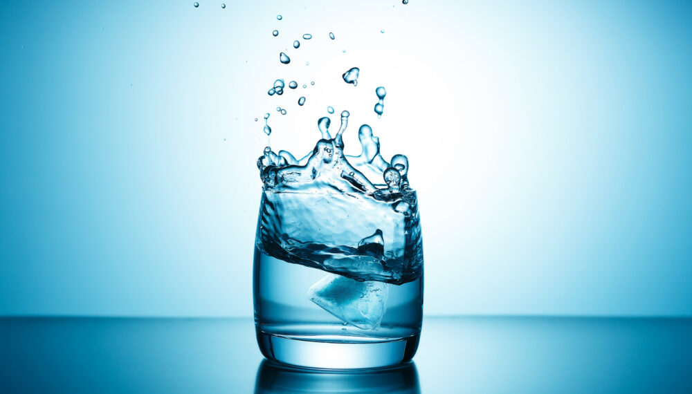 Pure water splashing out of glass on blue background